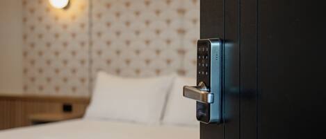 A hotel room with a bed, a wall-mounted light, and a modern door lock.