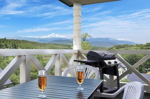 Un balcón con una copa de vino, una parrilla y vistas a una cadena montañosa.