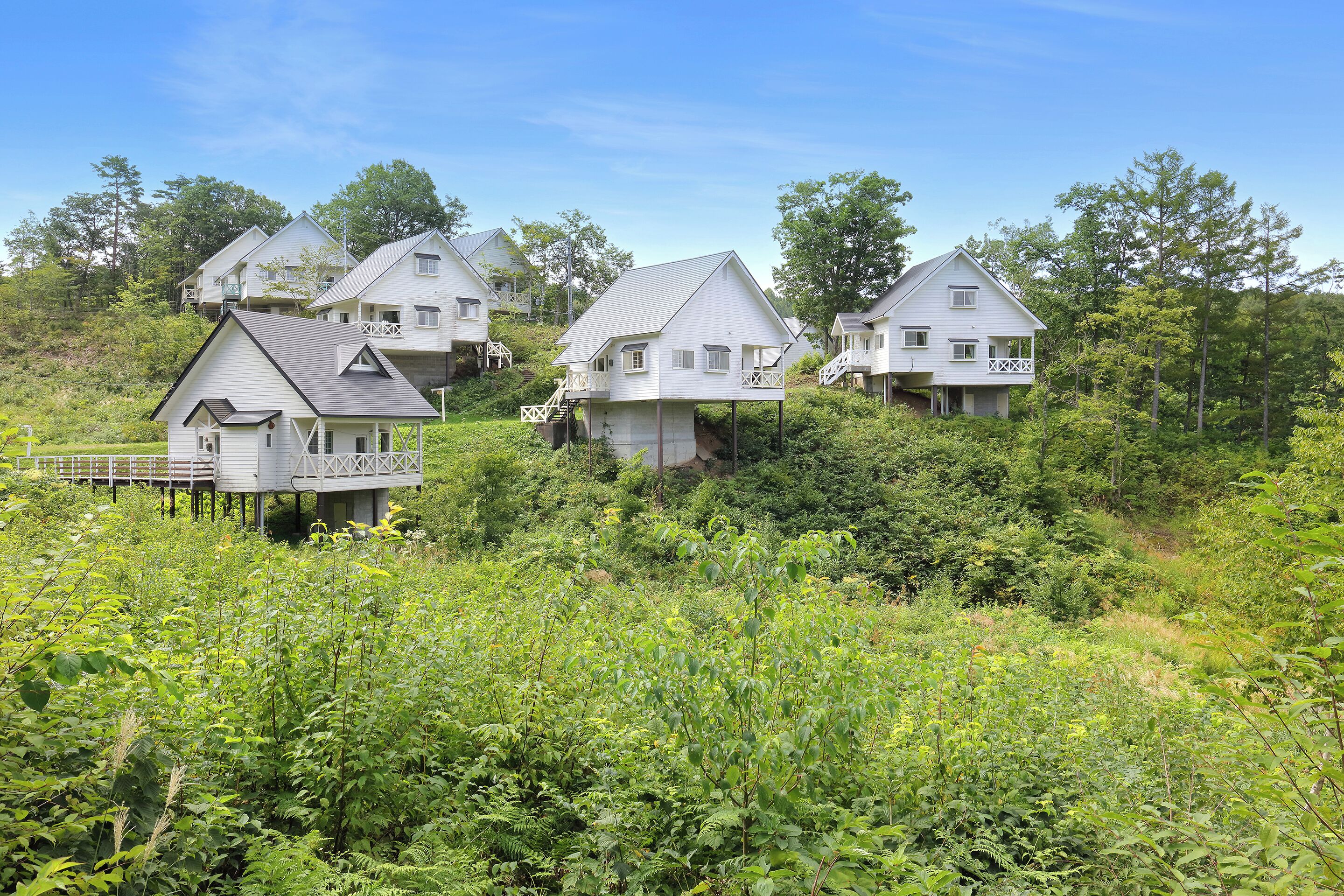 A cluster of white houses with balconies, surrounded by dense greenery.
