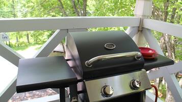 A barbecue grill on a white deck with a view of trees in the background.