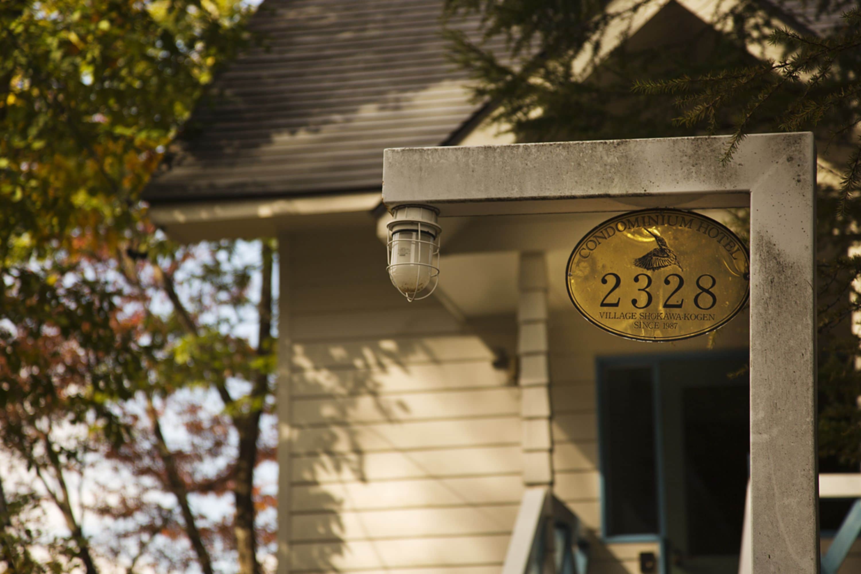 A house number sign with the number 2328 and the name "Condominium Hotel Village Shokawa-Kogen" on a building facade.