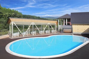 An outdoor swimming pool with a covered seating area, a building with a sloped roof, and a mountain in the background. - Resort Villa Takayama (Takayama)