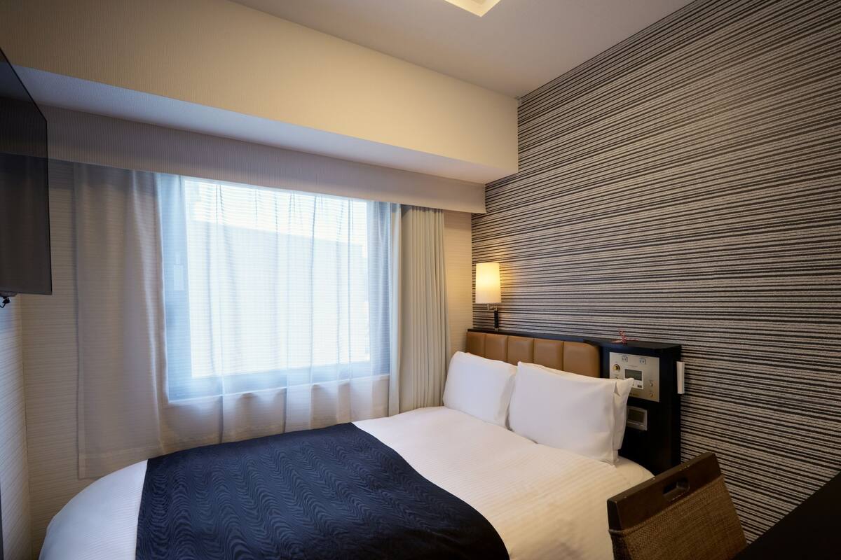Une chambre d’hôtel avec un lit, une table de chevet, une lampe et une fenêtre avec des rideaux.