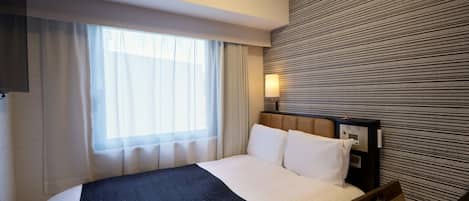 Una habitación de hotel con cama, mesita de noche, lámpara y ventana con cortinas.