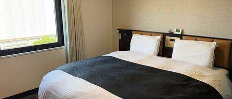 Quarto de hotel com uma cama, painel de controle e janela com cortinas.