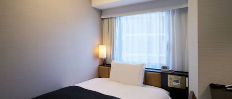 A hotel room with a bed, a nightstand, a lamp, a window with curtains, and a thermostat.