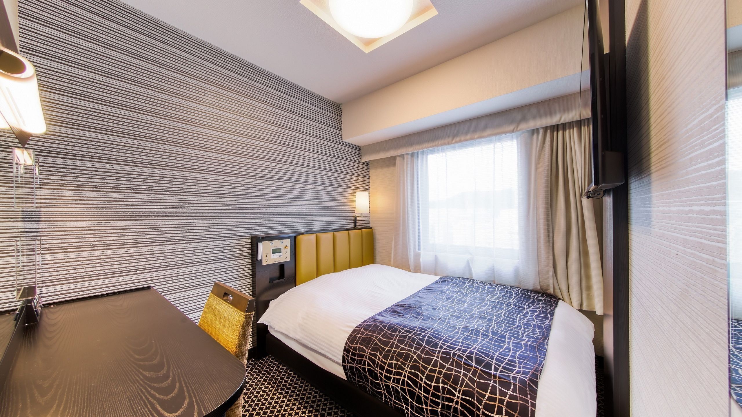 Une chambre d’hôtel avec un lit, une table de chevet, une lampe et une fenêtre avec des rideaux.