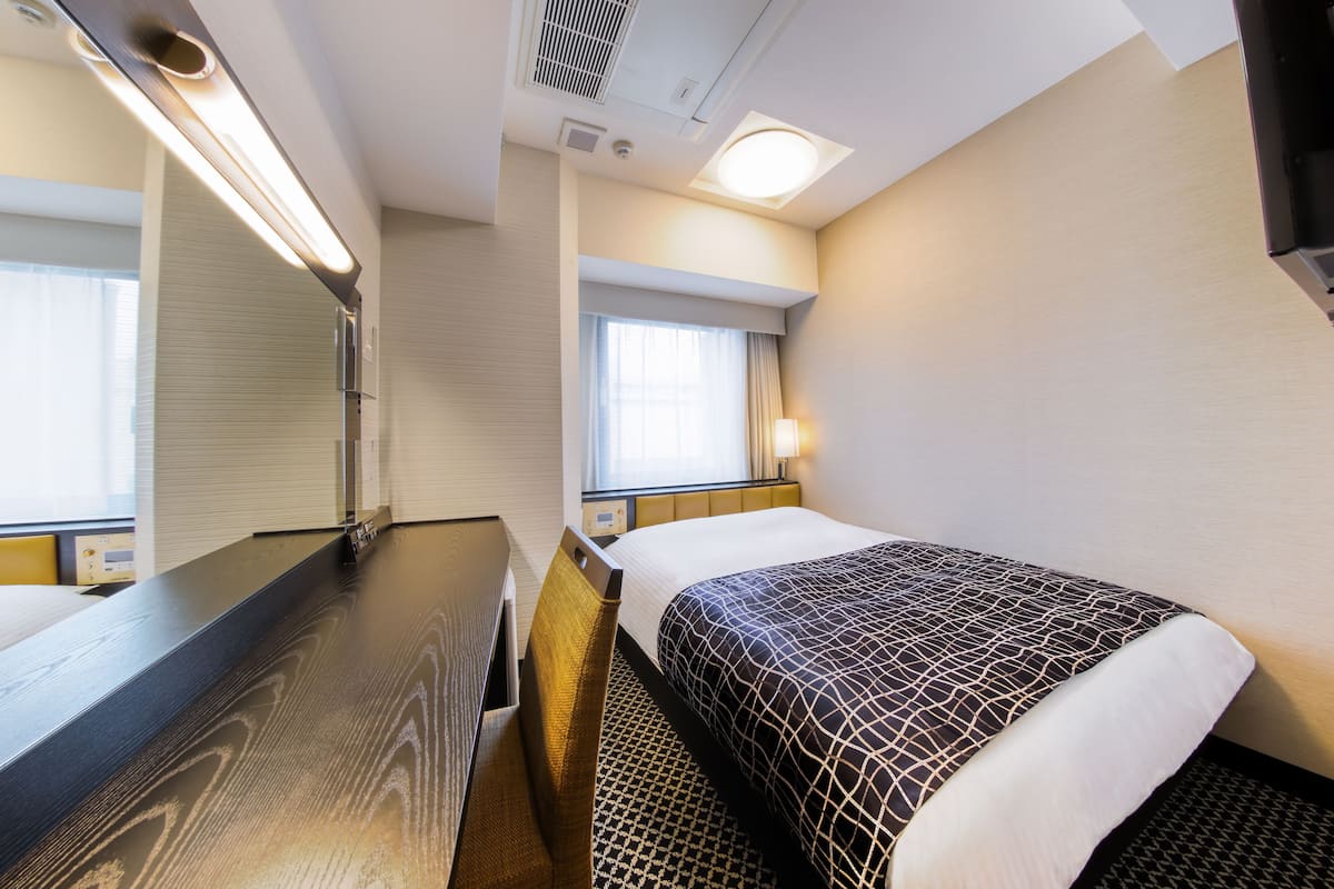 Une chambre d’hôtel avec un lit, un bureau, un miroir et une fenêtre avec des rideaux.