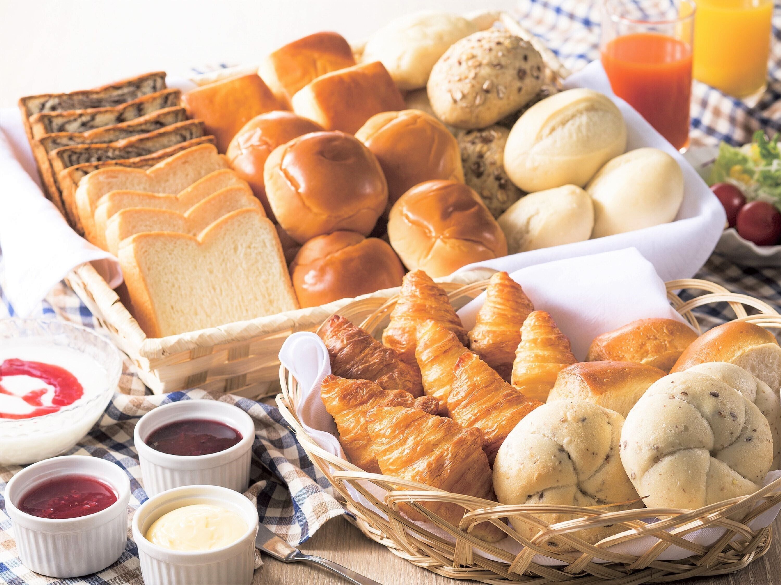 Una selezione di pane e dolci, tra cui croissant e panini, disposti su un tavolo con tovaglia a scacchi.
