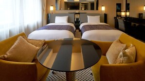 Habitación de hotel con dos camas, una mesita y dos sillones. Hay un espejo grande sobre las camas y un televisor en la pared.