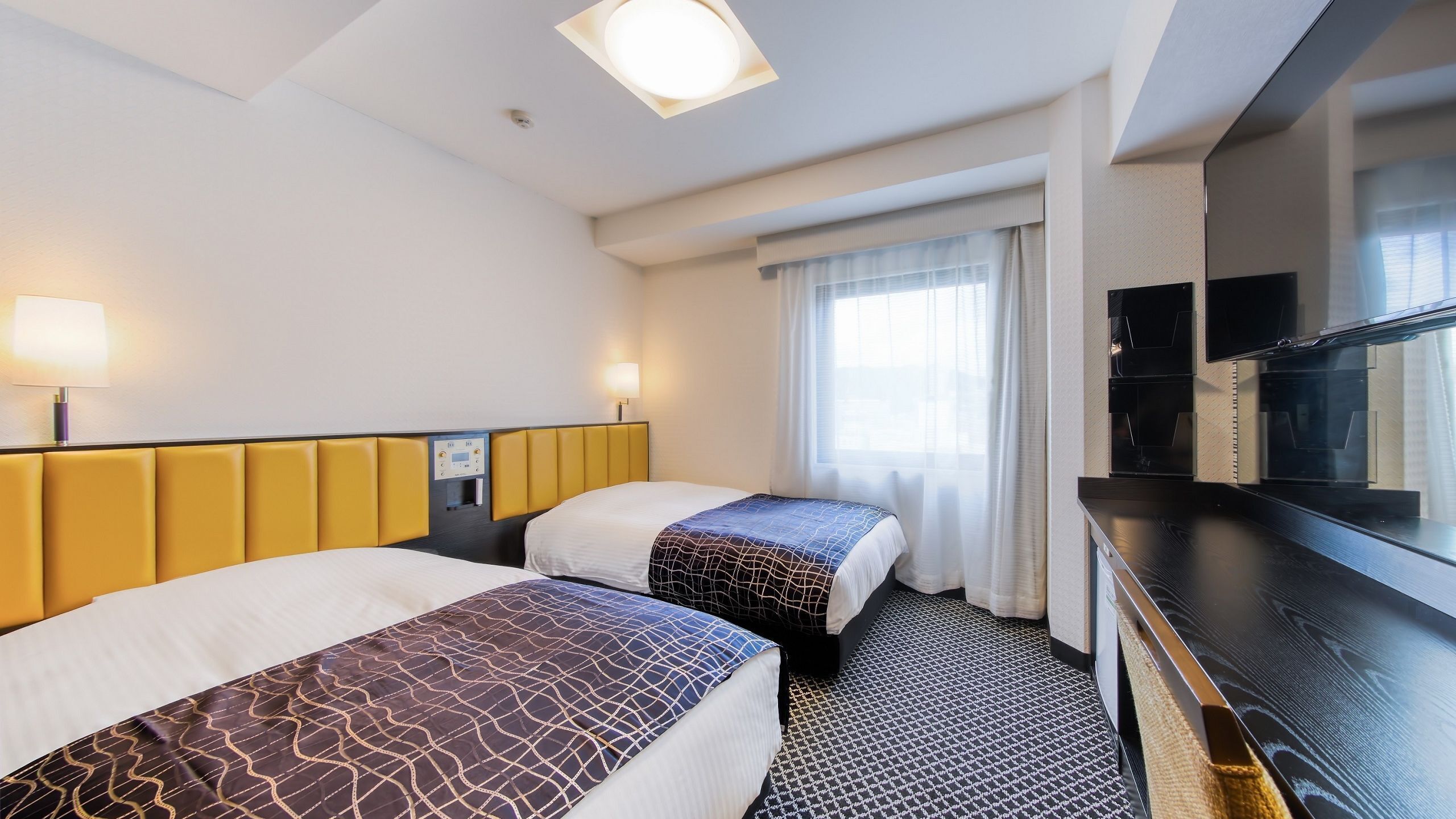 Une chambre d’hôtel avec deux lits, un panneau de commande, une télévision et une fenêtre avec des rideaux.