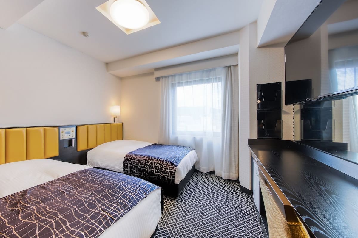 Une chambre d’hôtel avec deux lits, un panneau de commande, une télévision et une fenêtre avec des rideaux.