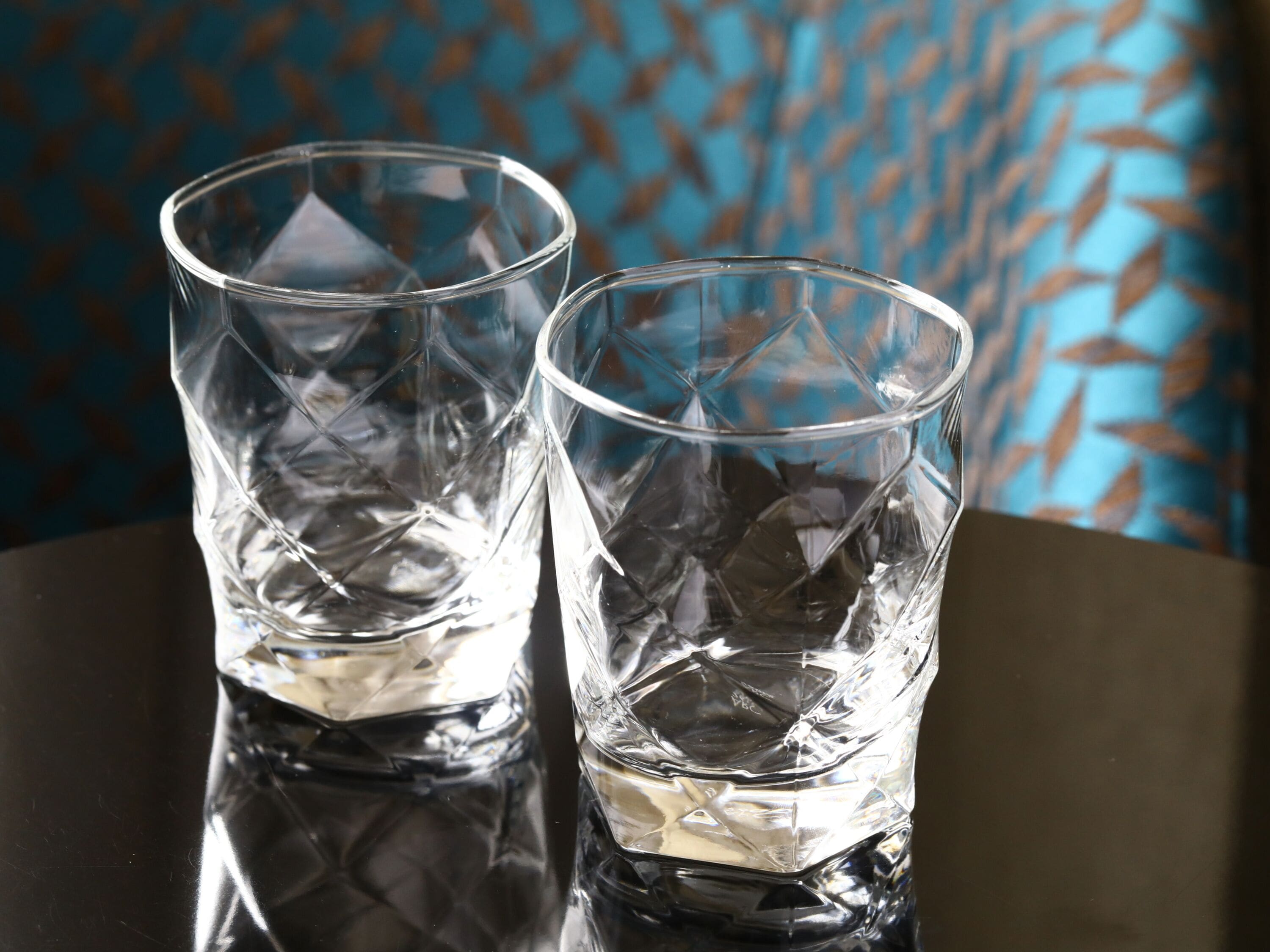 Deux verres transparents en verre, posés sur une surface réfléchissante.