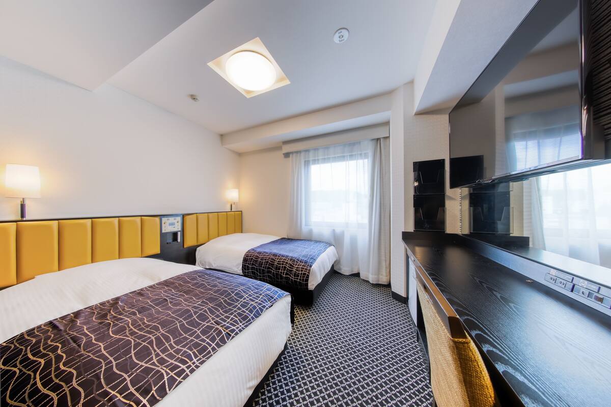 Une chambre d’hôtel avec deux lits, un téléviseur à écran plat, un bureau et une fenêtre avec des rideaux.