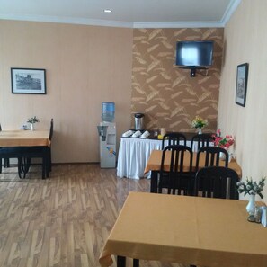 A dining area with tables and chairs, a water dispenser, a television mounted on the wall, and framed pictures on the walls.