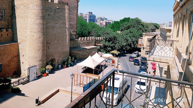 Un'antica torre in pietra con merlature, adiacente a un'area pavimentata con una tenda bianca e piante in vaso.