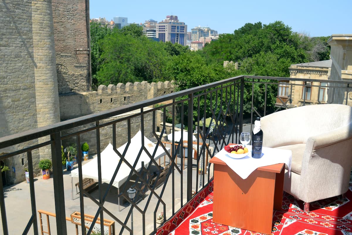 Un balcon avec une chaise, une table avec une bouteille et un verre, et une vue sur le paysage urbain et la verdure.