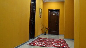 Un corridoio con pareti gialle, due porte in legno e un tappeto rosso con motivi decorativi.