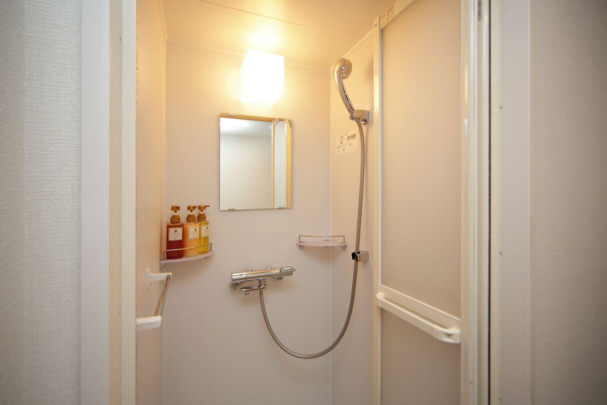 A bathroom with a shower, a mirror, and a shelf with toiletries.