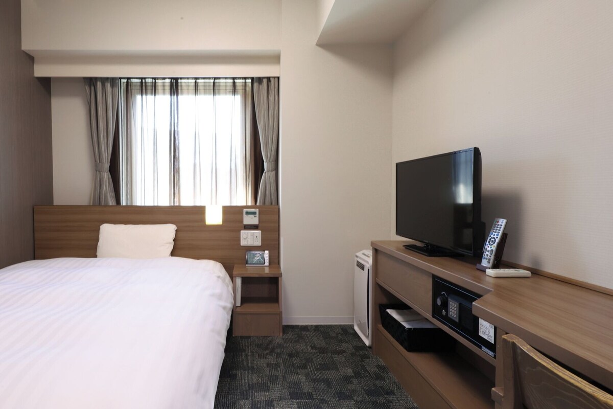 Een hotelkamer met een bed, een televisie, een nachtkastje, een verwarming en gordijnen.