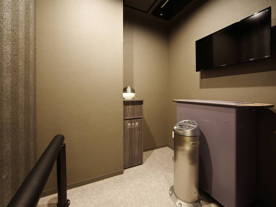 A hotel hallway with a trash bin, a small cabinet with a light, and a mounted television.