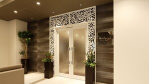 Zona de recepción con diseño moderno, que incluye una entrada con puerta de vidrio, un mostrador de recepción y plantas en macetas.