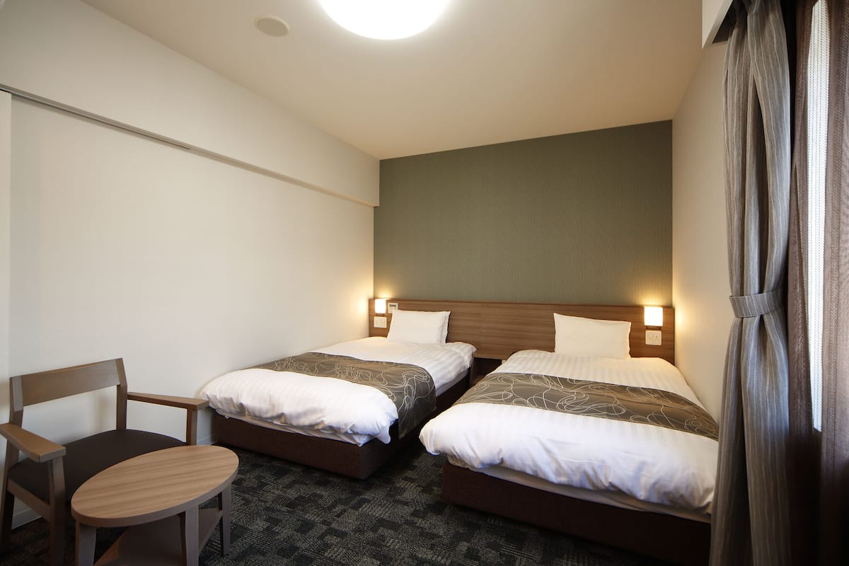 A hotel room with two beds, a wooden chair, and a small table.