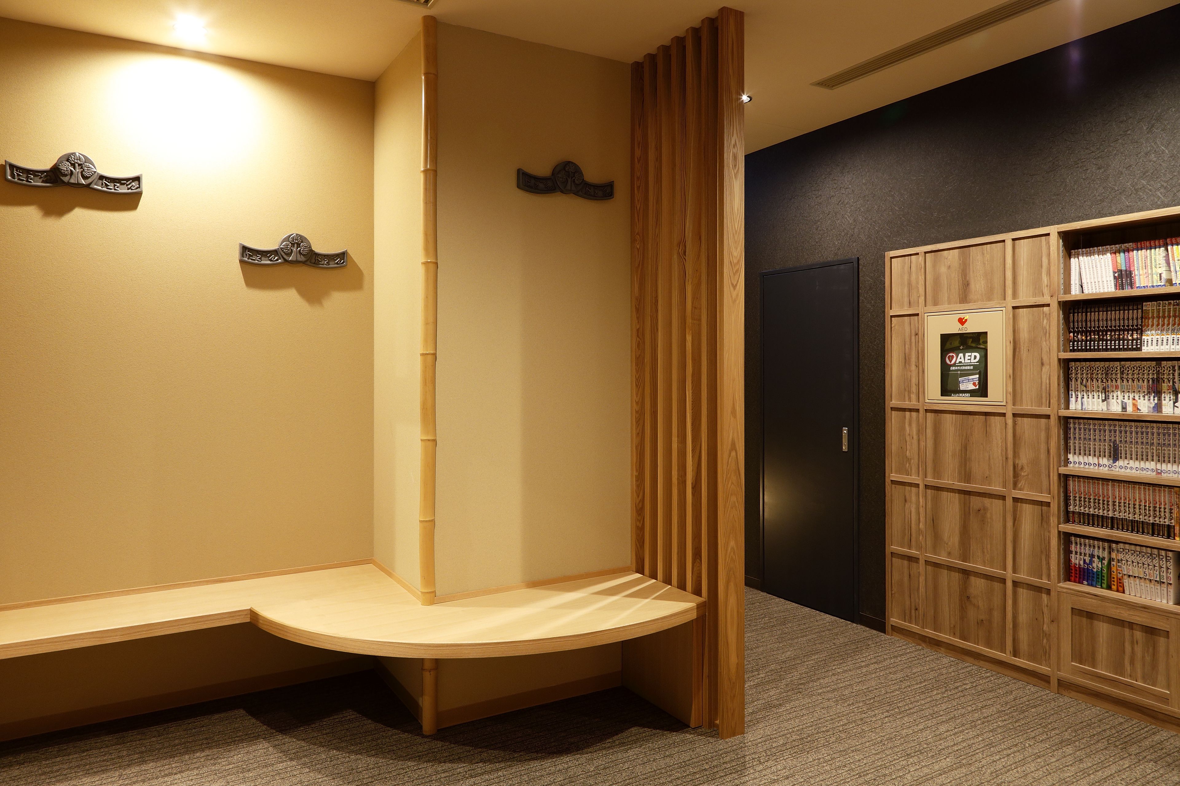 A reception area with a wooden bench, a bookshelf with books, and a wall-mounted AED sign.