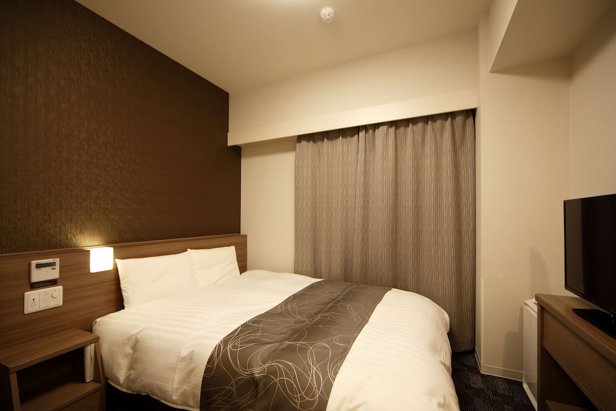 A hotel room with a bed, bedside table, TV, and curtains.
