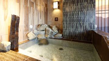 A stone hot tub with a wooden wall and a metal fence.
