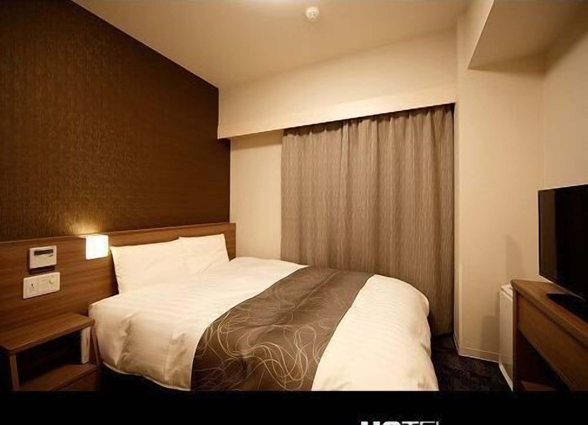 Quarto de hotel com cama, mesas de cabeceira, televisão e janela com cortinas.