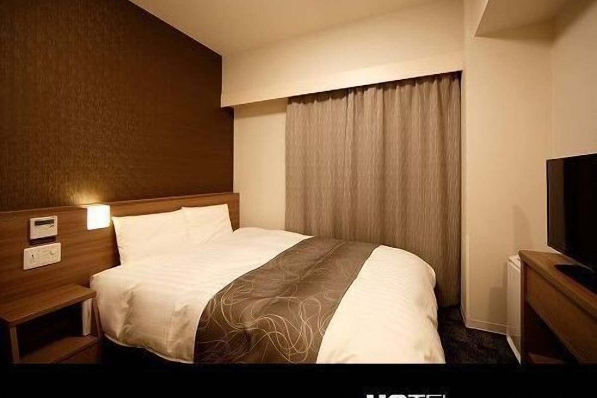 A hotel room with a bed, bedside tables, a TV, and a window with curtains.