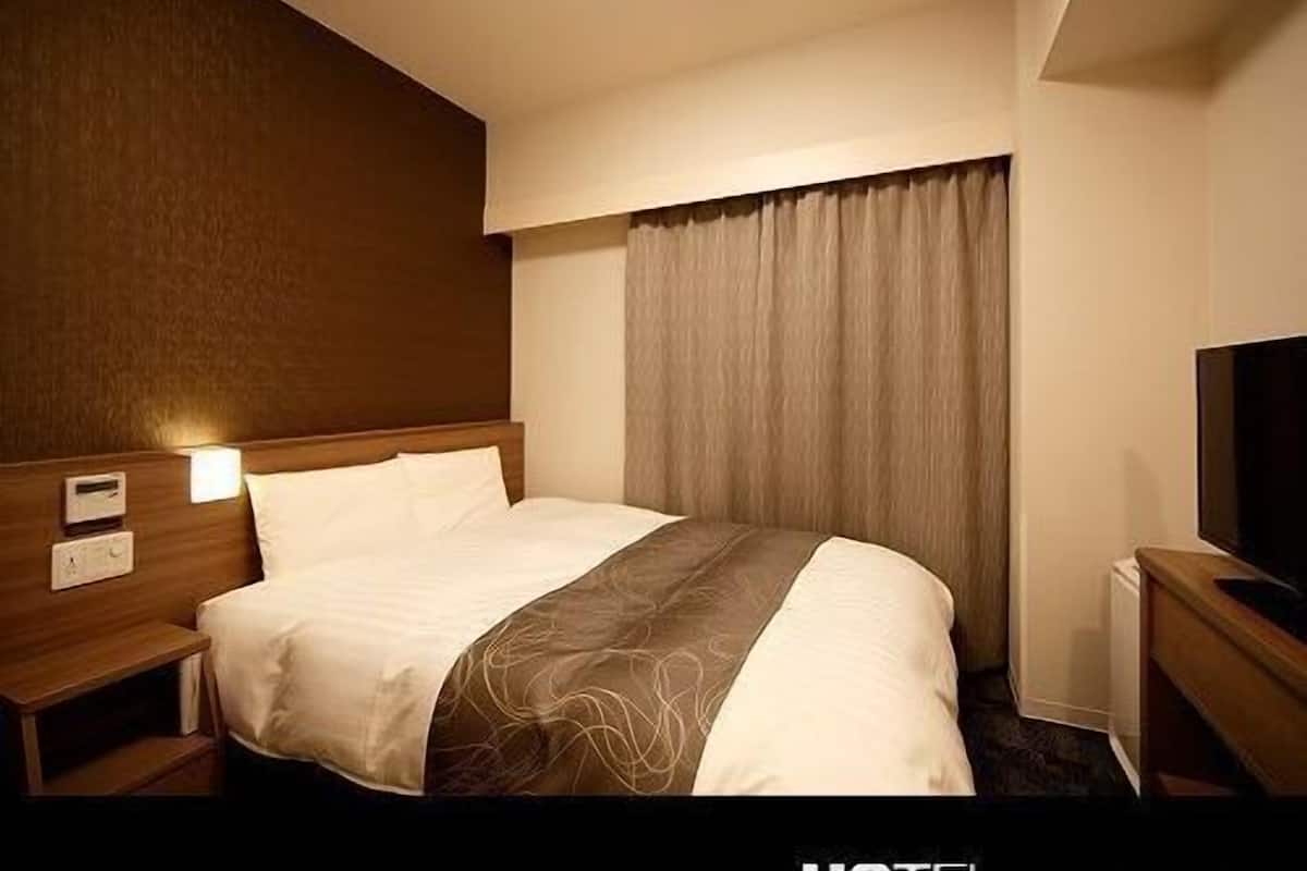 Une chambre d’hôtel avec un lit, des tables de chevet, une télévision et une fenêtre avec des rideaux.