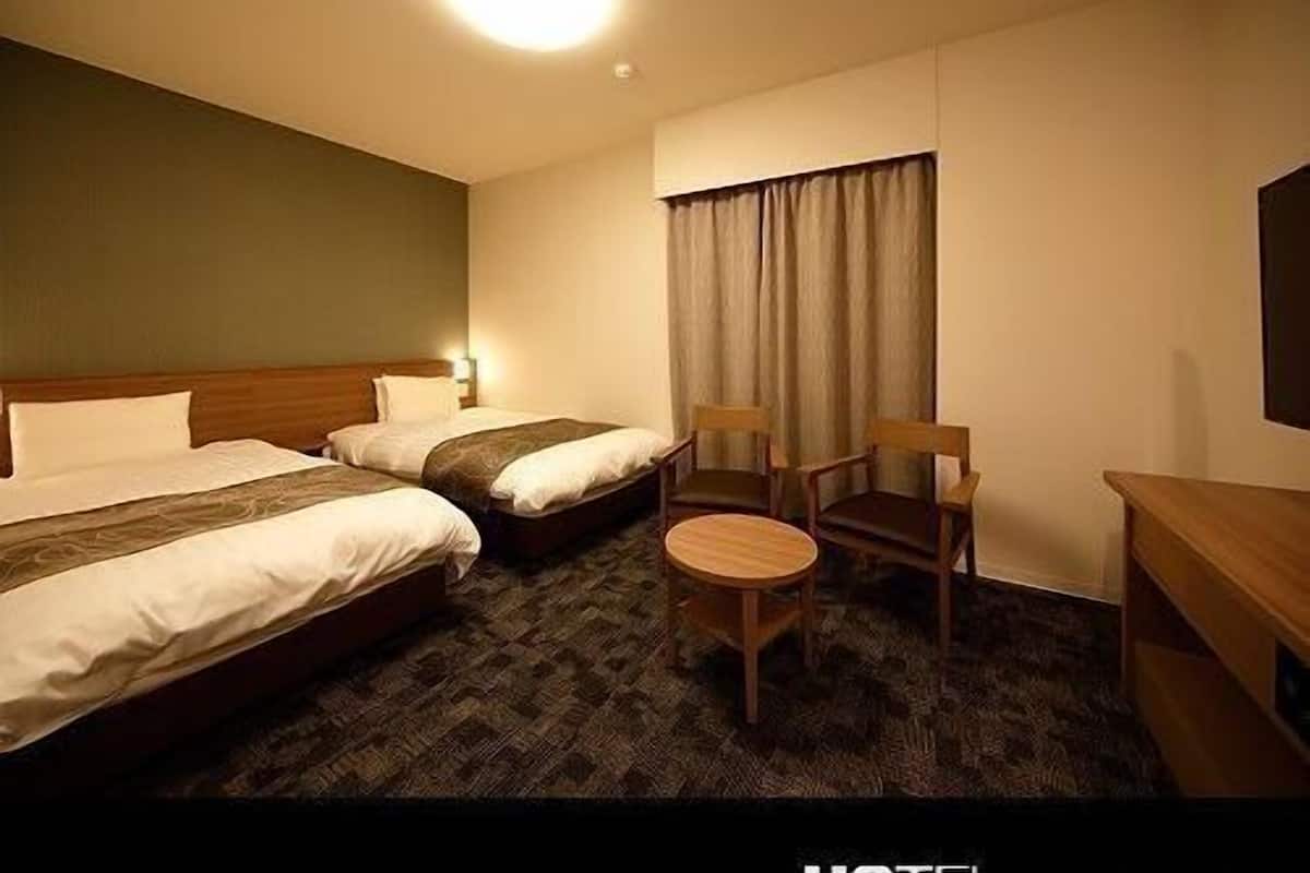 A hotel room with two beds, a small round table, two wooden chairs, a desk, and a large window with curtains.