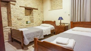 Une pièce avec deux lits en bois, un mur en pierre, une petite étagère et une table de chevet avec une lampe.