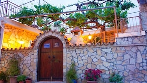 Un bâtiment en pierre avec une porte en bois, des plantes en pot et une enseigne indiquant qu’il s’agit d’une « Maison OLYMPIAC ».