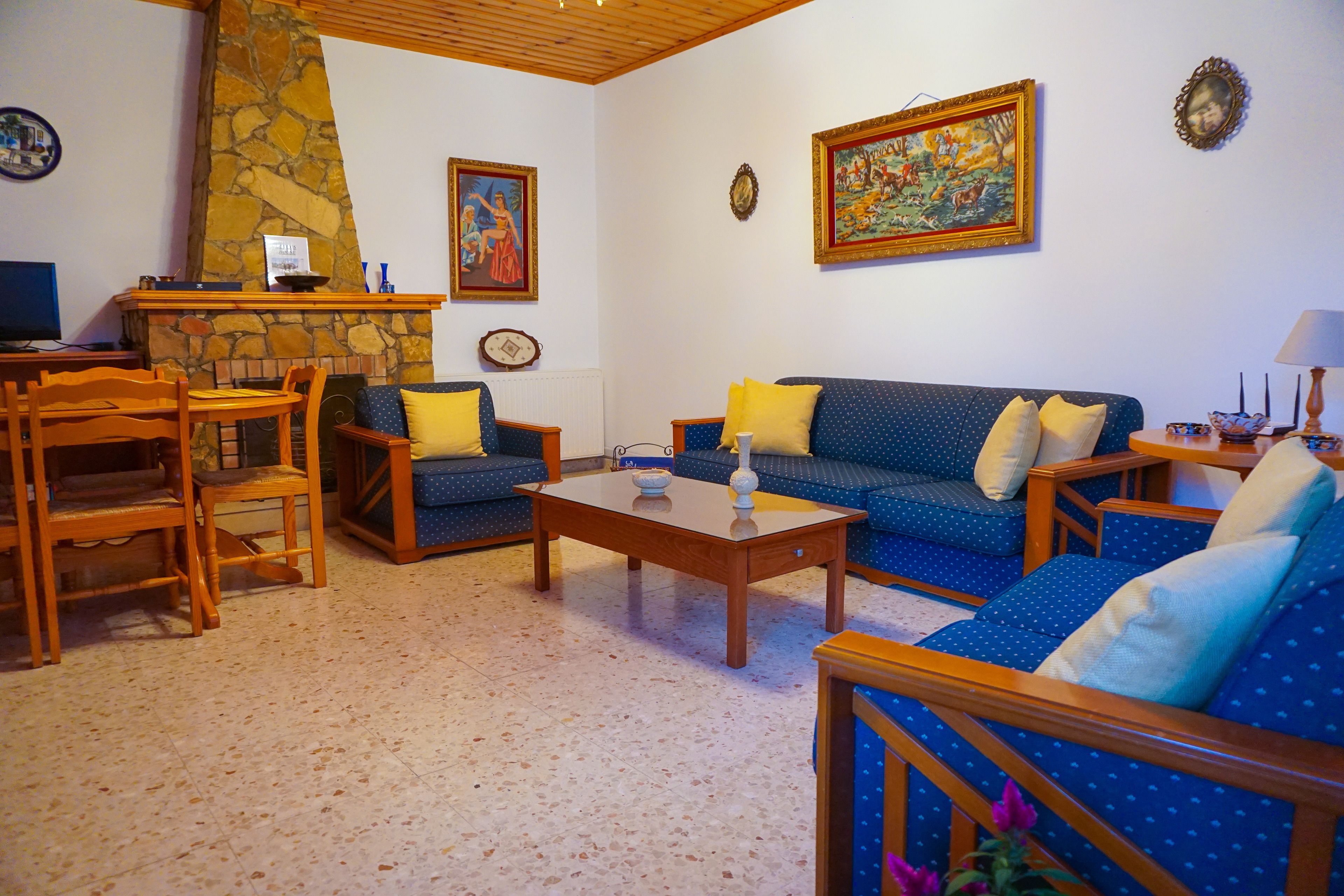Uma sala de estar com lareira de pedra, sofá azul, cadeiras de madeira e mesa de centro.