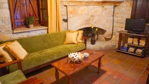 A cozy living room with a stone fireplace, a green sofa, a wooden coffee table, and a bookshelf. - Omodos Village Houses (Omodos)