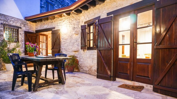 A stone building with a wooden table and chairs, large wooden doors, and a stone floor. - Omodos Village Houses (Omodos)