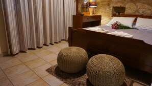 A bedroom with a wooden bed, a nightstand with lamps, a stone wall, and a curtain. - Omodos Village Houses (Omodos)