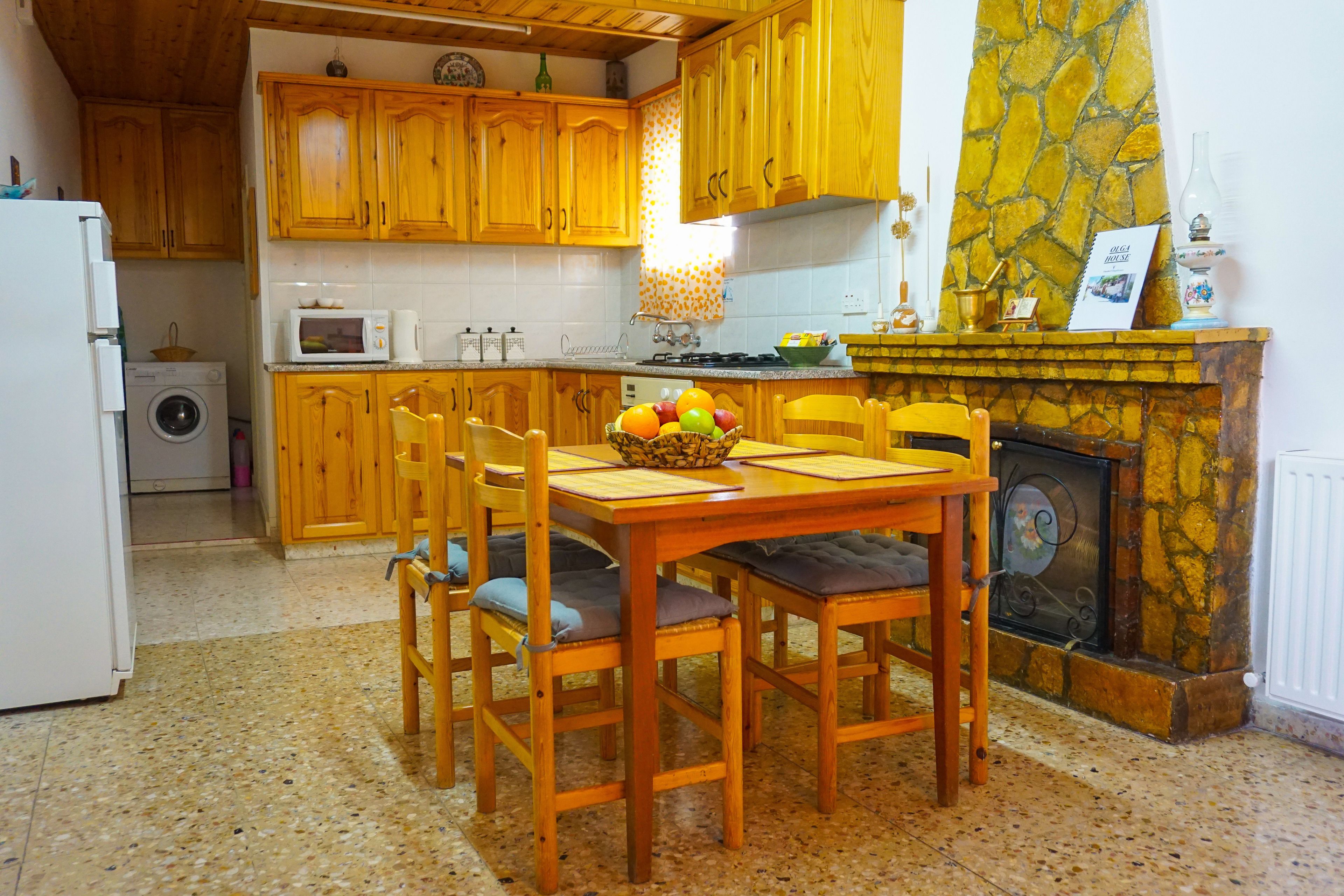A kitchen with wooden cabinets, a dining table with chairs, a washing machine, a microwave, and a fireplace.