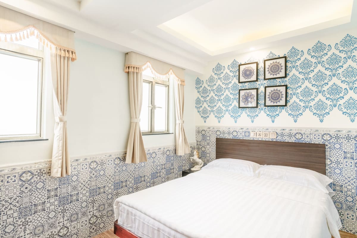 A bedroom with a patterned tile wall, a bed with white bedding, and a nightstand with a lamp.