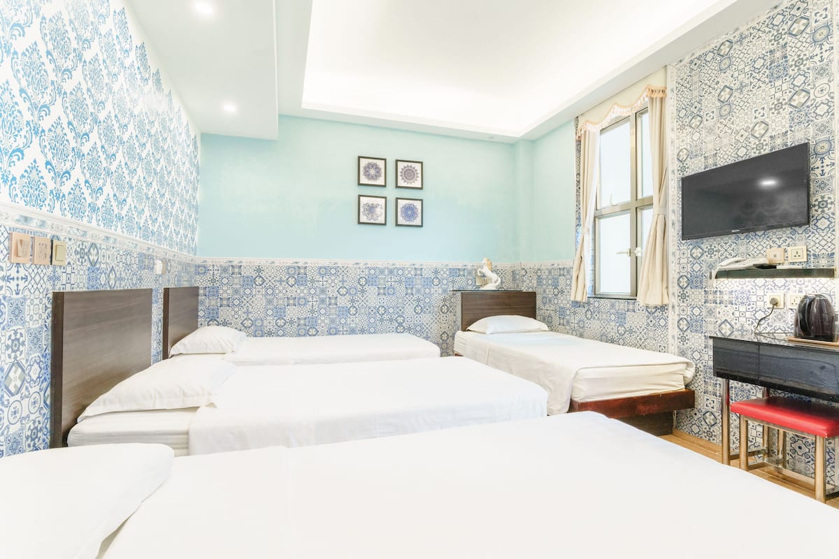 A hotel room with three beds, a TV, and a desk with a red bench.