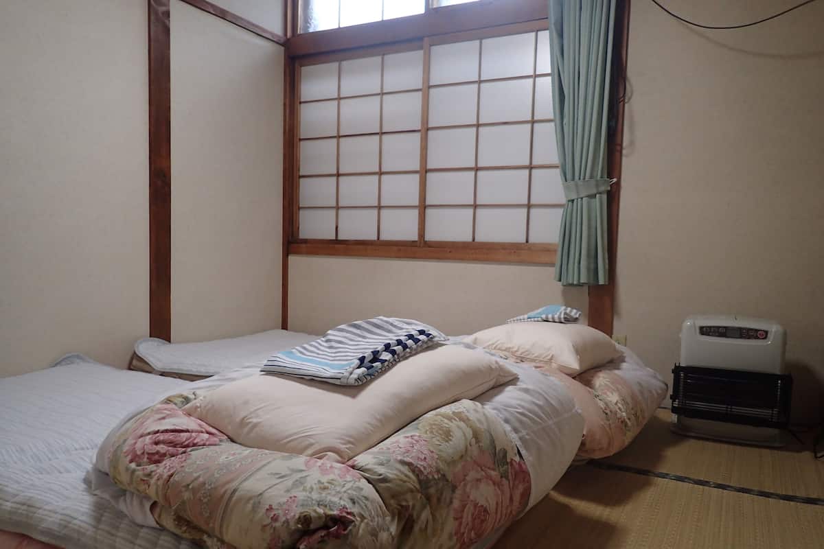 Une pièce de style japonais traditionnel, avec un sol recouvert de tatamis, un futon servant de lit, un paravent shoji et un radiateur portatif.