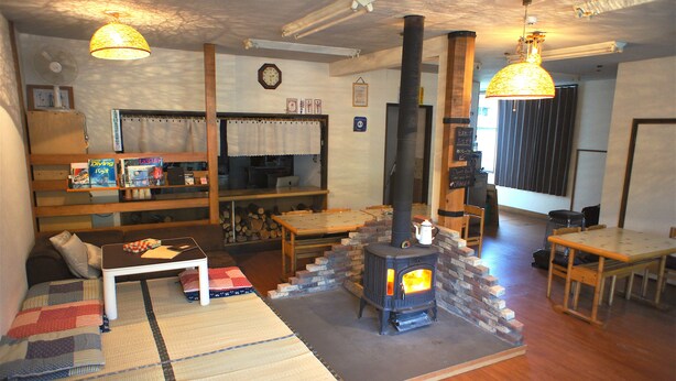 A cozy living room with a fireplace, wooden furniture, and a dining area. - Guest House Shikotsu Kamui - Hostel (Chitose)