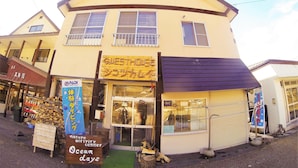 A two-story building with a yellow facade and a blue awning. There is a sign for a guesthouse and a sign for a nature activity center. - Guest House Shikotsu Kamui - Hostel (Chitose)