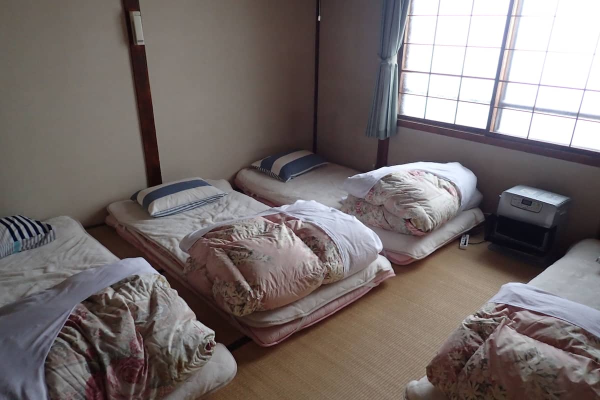 Une chambre de dortoir avec trois lits, un petit bureau avec une imprimante et une fenêtre donnant sur l’extérieur.