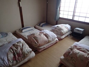A dormitory room with three beds, a small desk with a printer, and a window with a view of the outside.