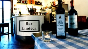A bar named Bar Enoteca with a checkered tablecloth, two bottles of wine, and a lit candle on the table.