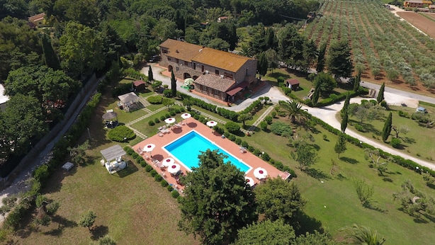 An aerial view of a villa with a swimming pool, surrounded by lush greenery and agricultural fields.